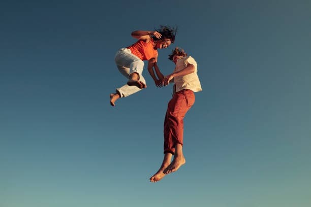 Two friends leaping into the air together against a clear blue sky